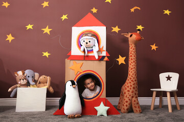 Cute little boy playing with cardboard rocket and toys at home. Child's room interior