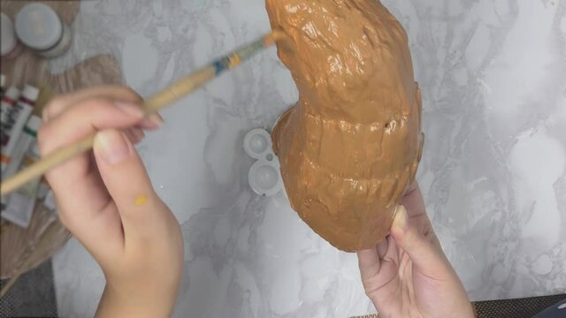 Girl dips brush into palette of acrylic paint and then applies it to antler. Women's hands paint white primed horn with brown color. Preparation of props for cosplay. Handicrafts concept.