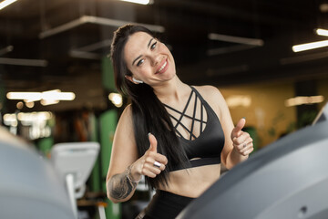 Fototapeta na wymiar Young smiling fitness woman showing thumbs up in the gym