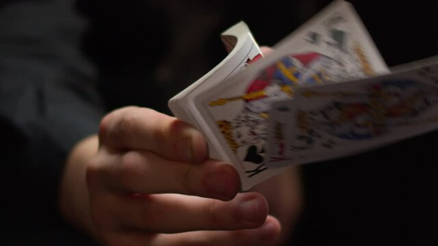 Person hand holds deck of flying playing cards on black background in dark studio extreme close view motion around