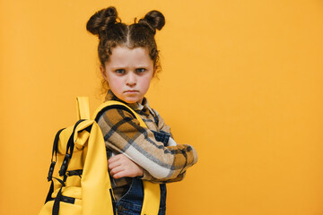 Portrait of angry sad little schoolgirl, crossed arms looking to camera, does not want to go to...