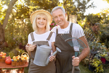 Lovely senior spouses holding gardening tools, working in garden at sunny day, woman with watering can, man with rake © Prostock-studio
