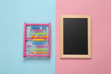Mini chalk board and toy abacus on pink blue background. Top view