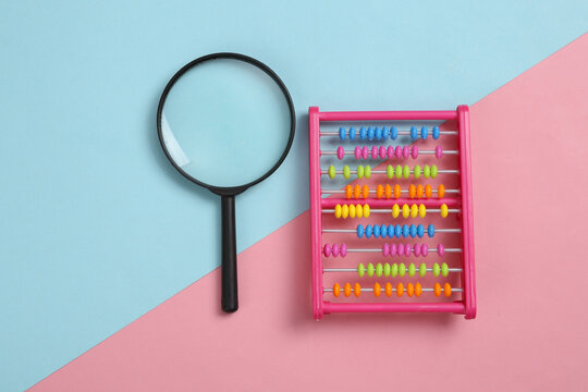 Magnifying glass and toy abacus on pink blue background