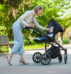 Obraz premium Cute caring mother with little daughter in a stroller walks in the park