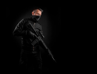 A man in dark clothes holds an automatic carbine in his hands. The face is covered with a mask,...