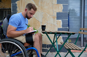 Young man in a wheelchair writing in his diary on a terrace