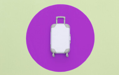 Travel concept. Mini plastic travel suitcase on pastel background with pink circle. Minimal style. Top view, flat lay