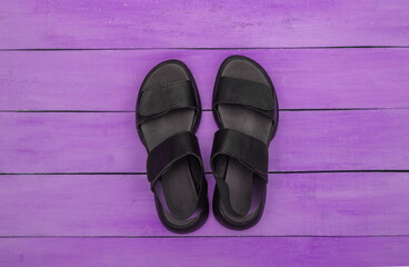 Feminine leather black sandals on purple wooden background. Top view