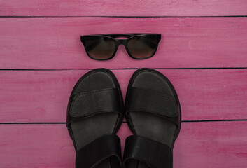 Fototapeta na wymiar Feminine leather black sandals and sunglasses on pink wooden background. Top view