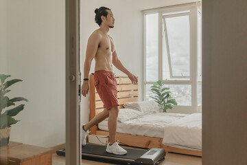 Asian man exercise by walking on the treadmill in his apartment.