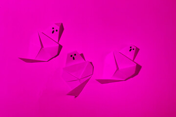 Origami ghosts in pink neon light. Halloween theme