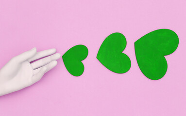 White mannequin hand and green hearts on pink background. Top view