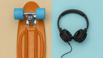 Cable black stereo headphones and cruiser board on a blue yellow background. Top view. Flat lay