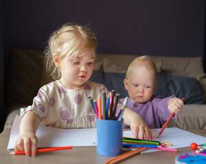 Adorable little girl with golden hair and cute baby boy drawing with colored pencils while sitting at table, older sister playing with small brother while enjoying leisure time together at home