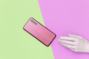 Plastic hand and smartphone on green-pink pastel background. Minimalism concept art. Top view