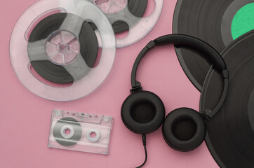 Retro vinyl records, audio magnetic reel, audio cassette and stereo headphones on pink background....