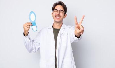 young hispanic man smiling and looking happy, gesturing victory or peace. chiropodist concept