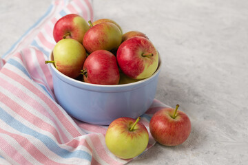 A pile of ripe red and green apples in a ceramic bowl. Harvest of juicy apples on a striped  cloth on a light textured background