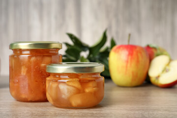 Tasty apple jam in glass jars on wooden table, space for text