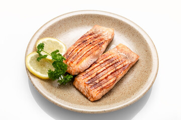 Grilled salmon fillet and lemon slices on a plate. White background. Healthy food. Isolate.