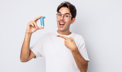 young hispanic man looking excited and surprised pointing to the side. asthma concept