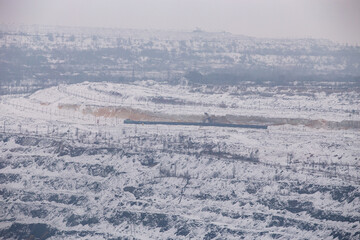 Fototapeta premium Iron ore quarry horizons covered with snow in winter, mining process in winter in cloudy weather