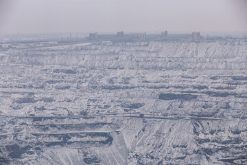 Iron ore quarry horizons covered with snow in winter, mining process in winter in cloudy weather