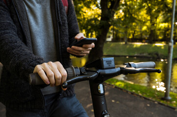 Man holding a phone and using mobile app for rent electronic scooter. Close-up. Modern eco urban transportation.