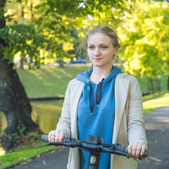 Obraz premium Woman holding steering wheel of black electronic scooter in autumn park. Close-up. Modern eco urban transportation.