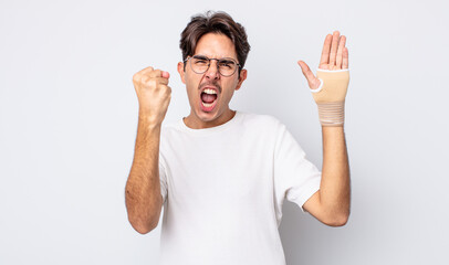 young hispanic man shouting aggressively with an angry expression. hand bandage concept