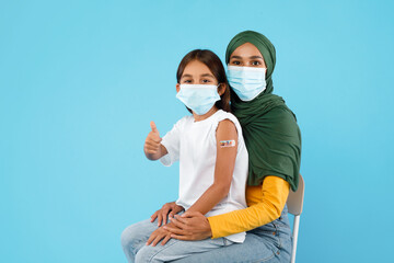 Vaccinated Islamic Mother And Daughter Gesturing Thumbs-Up Over Blue Background