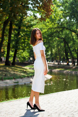 Young beautiful brunette girl in a white skirt posing in a summer park