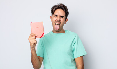 young hispanic man with cheerful and rebellious attitude, joking and sticking tongue out. 2022 planner concept