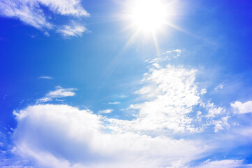 The bright sun in a blue sky with some clouds