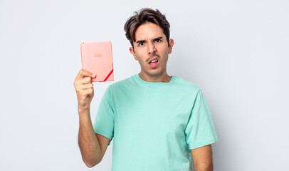 young hispanic man feeling puzzled and confused. 2022 planner concept