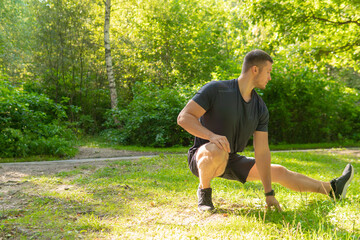 A young enduring athletic athlete is doing stretching in the forest outdoors, around the forest, oak trees.healthy exercise, workout athletic male, jogging Autumn energy cross, feet stretches