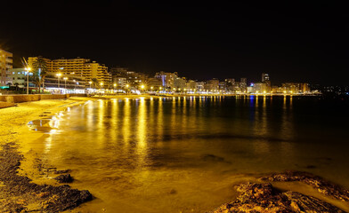 Beach at night with illuminated buildings and reflections of lights in the water. Calpe Alicante.