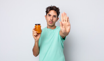 young hispanic man looking serious showing open palm making stop gesture. peach jelly concept