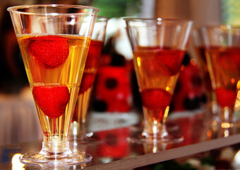 Yellow transparent cocktail with red strawberries in narrow triangular glasses, blurred background