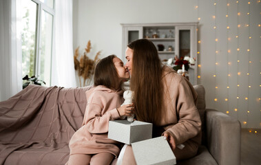 daughter and mom are sitting on the couch with an open gift and kissing