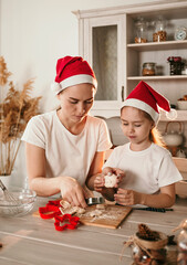 cheerful mom and daughter in Christmas hats play at the table in the kitchen