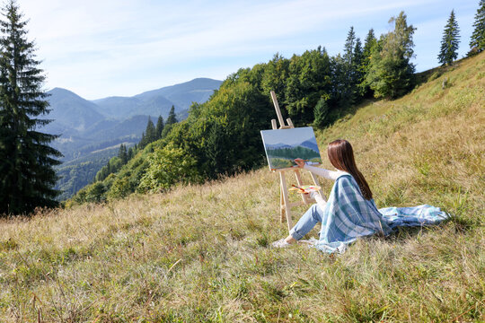 Young woman drawing on easel in mountains, back view. Space for text