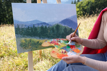 Young woman drawing on easel with brush outdoors, closeup
