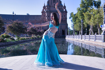 Middle-aged Hispanic woman in turquoise dress with rhinestones, doing belly dance figures. Belly dance concept.