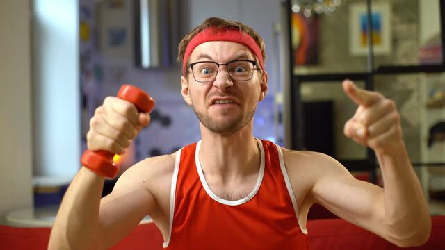 Portrait of funny geek with dumbbell screaming to camera. Sport motivation concept.