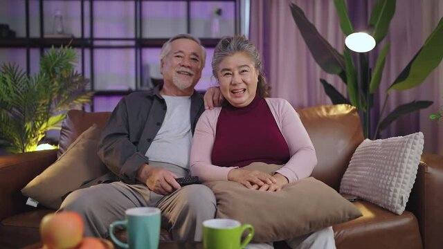 old retired age asian couple watching TV at home,old mature asian couple cheering sport games competition together with laugh smile victory on sofa couch at living room home isolation activity