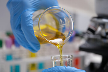 Chemist pouring edible oil from flask into test tube closeup
