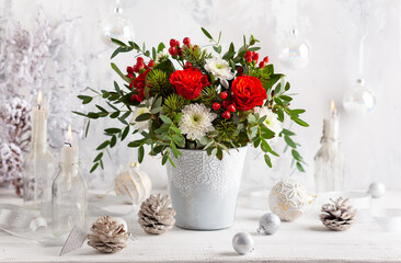 Obraz na płótnie Canvas Festive winter flower arrangement with red roses, white chrysanthemum and berries in vase on table. Christmas decorations for holiday.