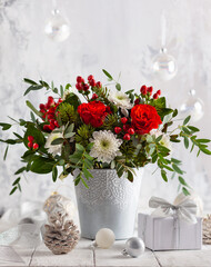 Festive winter flower arrangement with red roses, white chrysanthemum and berries in vase on table. Christmas decorations  for holiday.